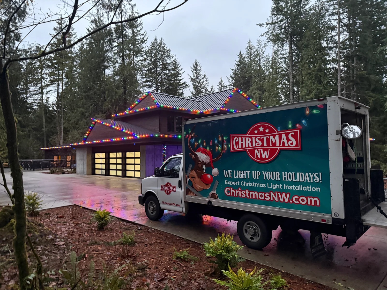 Christmas Northwest box truck beside a completed multicolor Christmas light installation at dusk